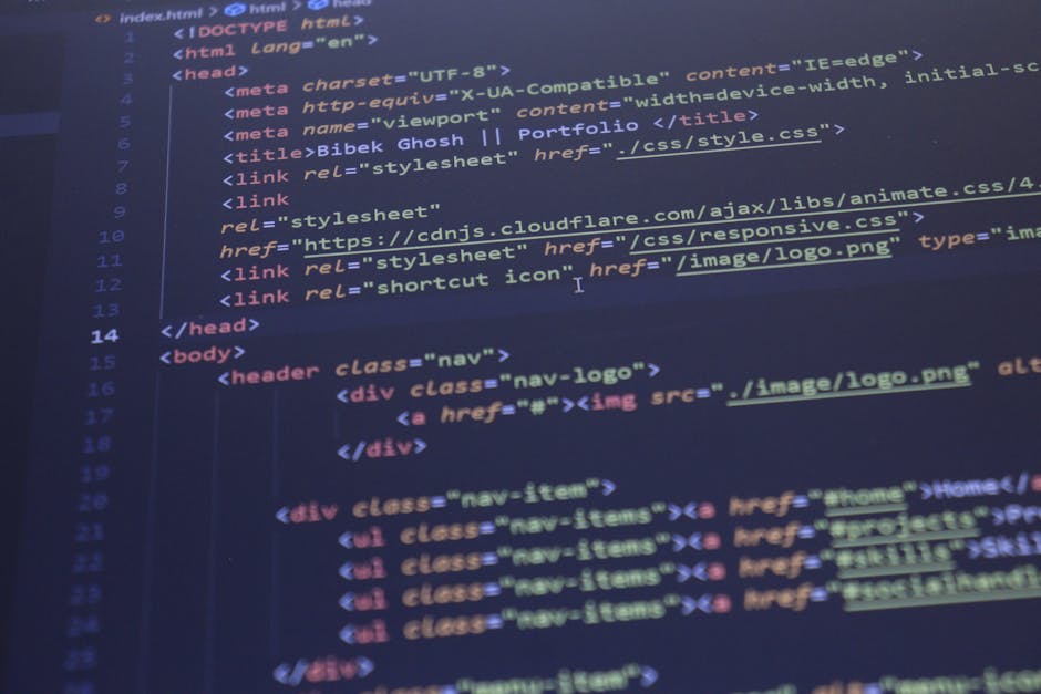 A close-up view of a person's hands typing on a laptop keyboard, which displays a dark-themed code editor with lines of multicoloured programming code. The laptop is positioned on a black table or des