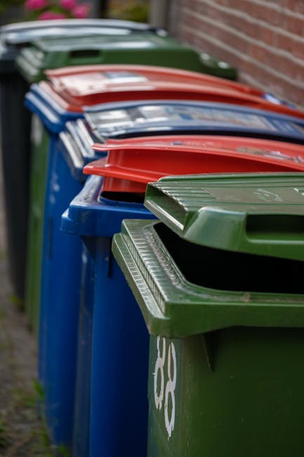 A close-up view of a mound of crushed aluminum beverage cans in various metallic shades, predominantly silver, with some featuring colorful branding, including red and blue elements. The cans are crum